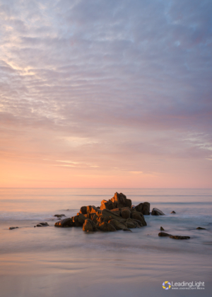 A rock on Guernsey's L'Ancresse Bay, side-lit by a warm sunset and surrounded by a rising tide.