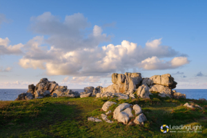 Cumulous clouds pass over rocks near Mont Cuet, L'Ancresse Common just before sunset.